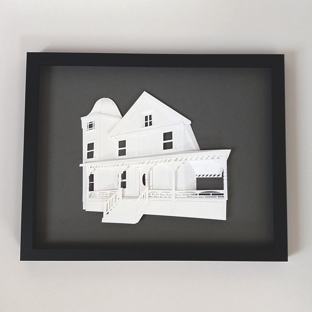 a paper cut of a house in a black frame