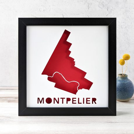 A map of Montpelier, Vermont cut out of white paper in a black frame with a red background