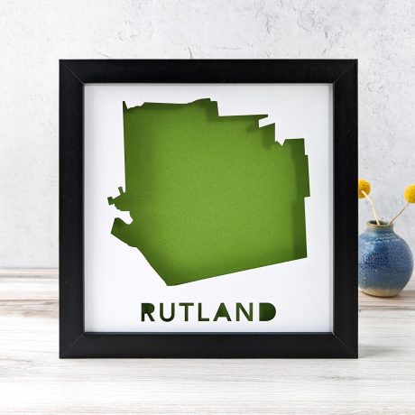 A map of Rutland, Vermont cut out of white paper in a black frame with a green background