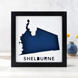 A map of Shelburne, Vermont cut out of white paper in a black frame with a navy background