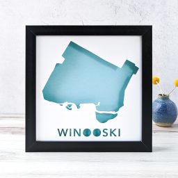 A map of Winooski, Vermont cut out of white paper in a black frame with a blue background