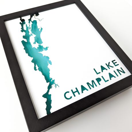 a black framed map of lake champlain cut out of white paper to reveal a blue background