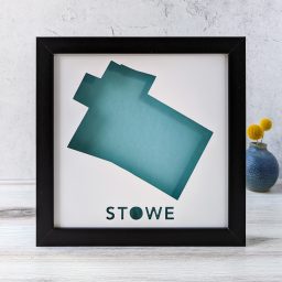 A map of Stowe, Vermont cut out of white paper in a black frame with a blue background