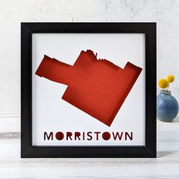 A map of Morristown, Vermont cut out of white paper in a black frame with a red background