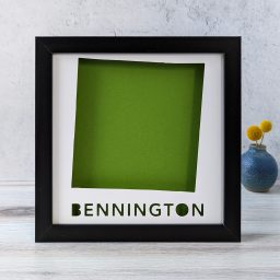 A map of Bennington, Vermont cut out of white paper in a black frame with a green background