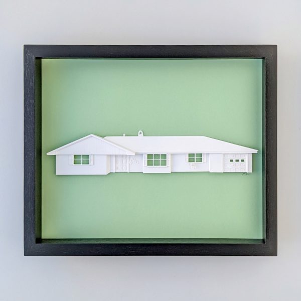 A portrait of a ranch style home sculpted out of white paper on a mint green background in a black frame