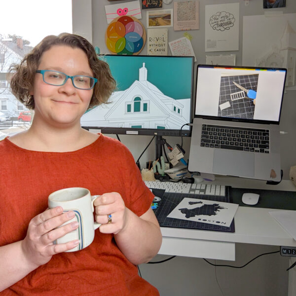 Artist Abigail McMurray holding a coffee cup in front of a computer