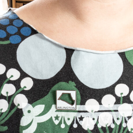 a close up of a person's neck wearing a shirt with flowers on it and an Arlington, MA Local Places pin