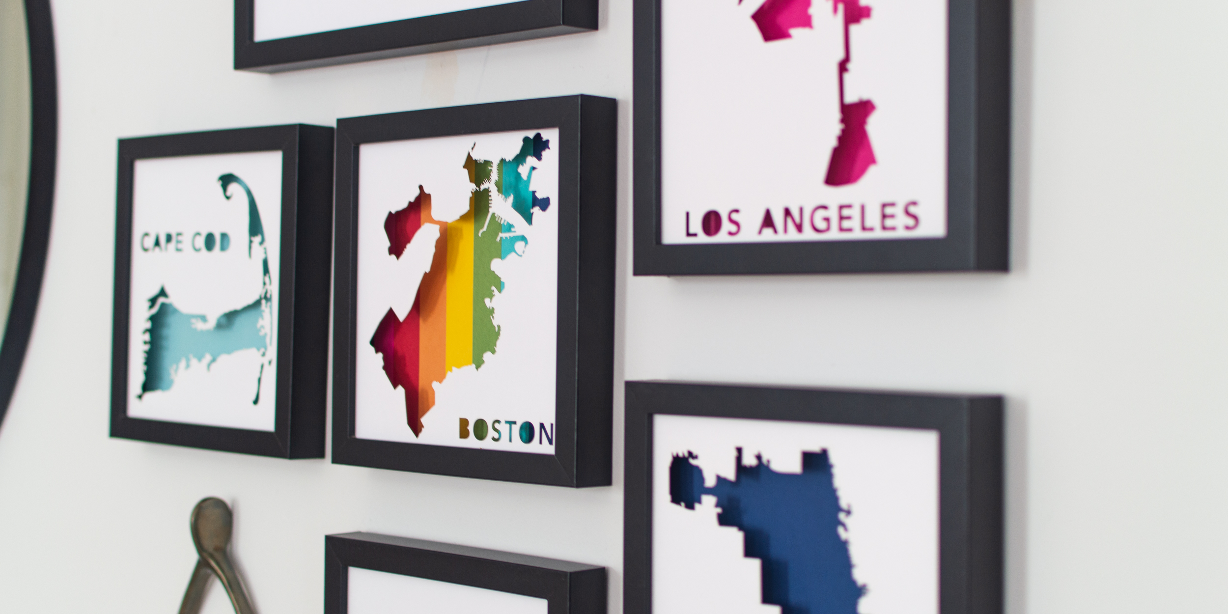 a wall with framed Paper Places maps of Cape Cod, Boston, Los Angeles, and Chicago