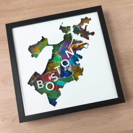 a framed map of Boston, MA cut from white paper, with a multi-colored collaged background and 3D letters spelling "Boston"