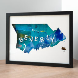 A framed map of Beverly, MA. The map is cut from white paper to reveal a collage of blue and green papers with the word "Beverly" spelled out of 3D paper letters