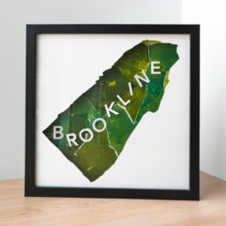 A framed map of Brookline, MA. The map shape is cut from white paper to reveal a green collaged background and 3D paper letters that spell "Brookline"