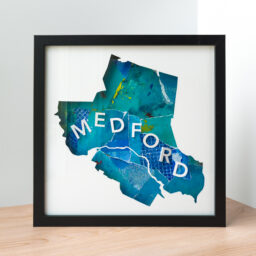 A framed map of Medford, MA. The shape of the city is cut from white paper to reveal a blue and green collaged background with 3D paper letters that spell "Medford"