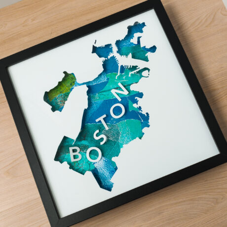 A square frame holding a blue and green collaged map of Boston, MA laying on a table