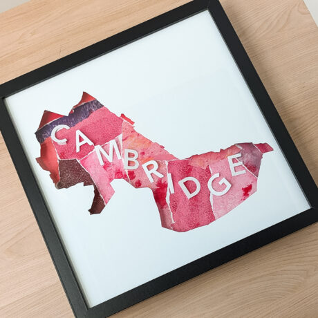 A square map of Cambridge, MA with a pink and red collaged textured background laying on a wooden table